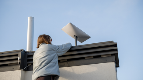 Person on a rooftop adjusting a white solar panel under a blue sky