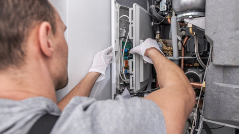Technician wearing gloves repairs wiring inside an open electrical panel.