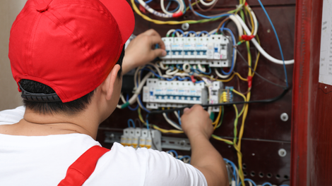 Technician in red cap wiring an electrical breaker panel with exposed cables