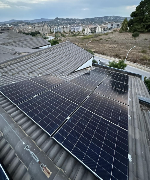 Pannelli solari installati su un tetto di tegole, con vista su un paesaggio suburbano sotto un cielo nuvoloso.