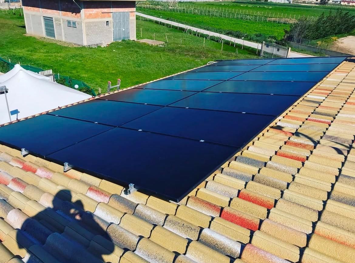 Pannelli solari installati su un tetto di tegole rosse, con paesaggio urbano e cielo azzurro sullo sfondo.