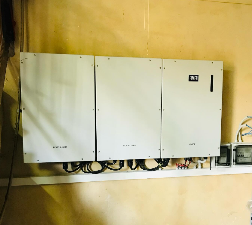 Tre quadri elettrici bianchi montati su una parete gialla con cavi e un piccolo display.