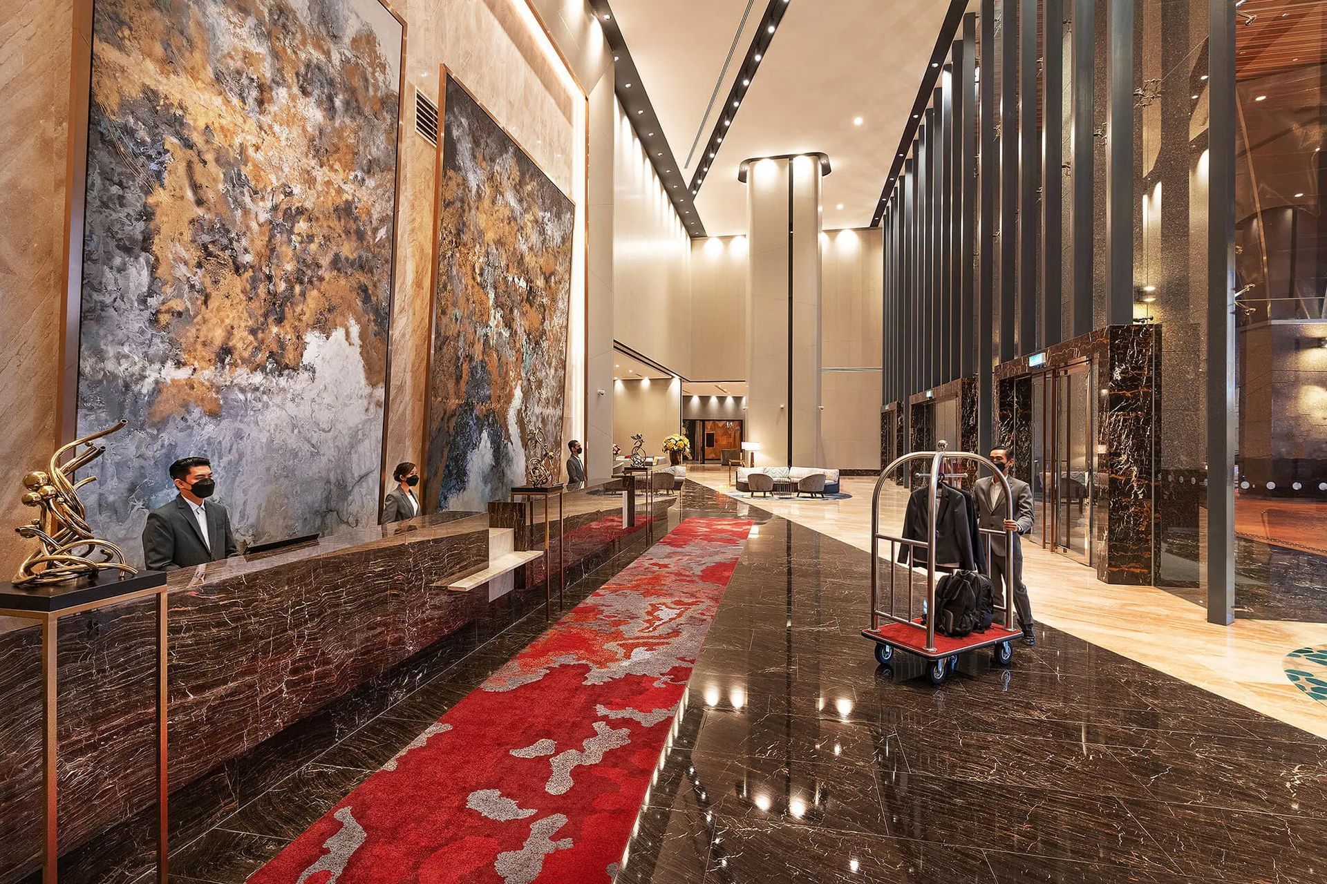 M World Hotel, a modern hotel lobby with red carpet, marble floor, tall art panels, and a luggage cart