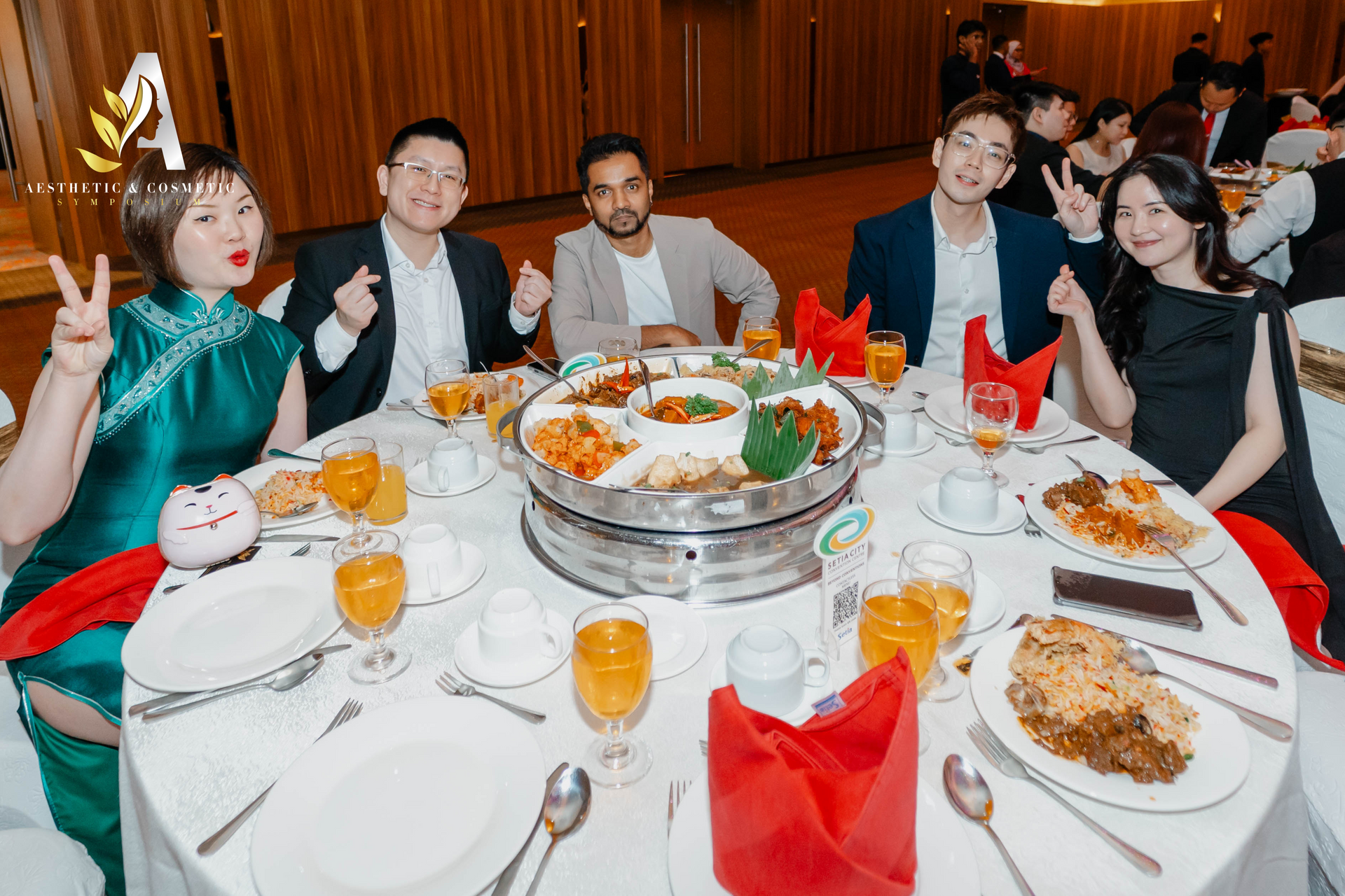 People at a round table, celebrating. Food and drinks. Some are making hand gestures.