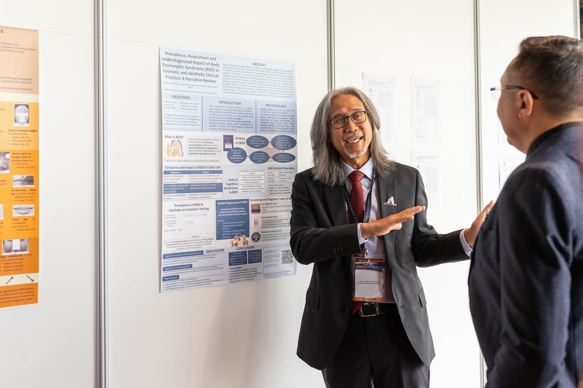 Two men discussing a poster presentation at a conference. One gestures, explaining the content.