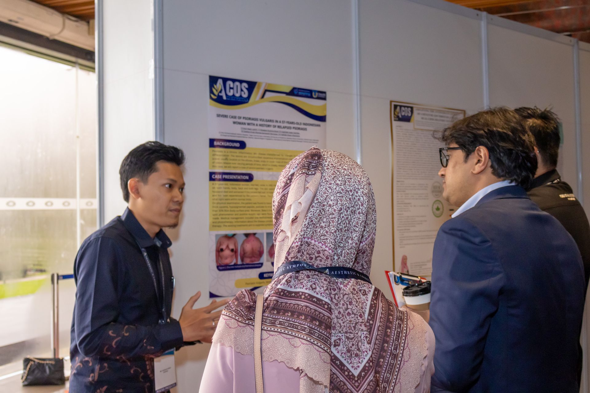 A man explains a poster to two people. The poster has blue and yellow accents.