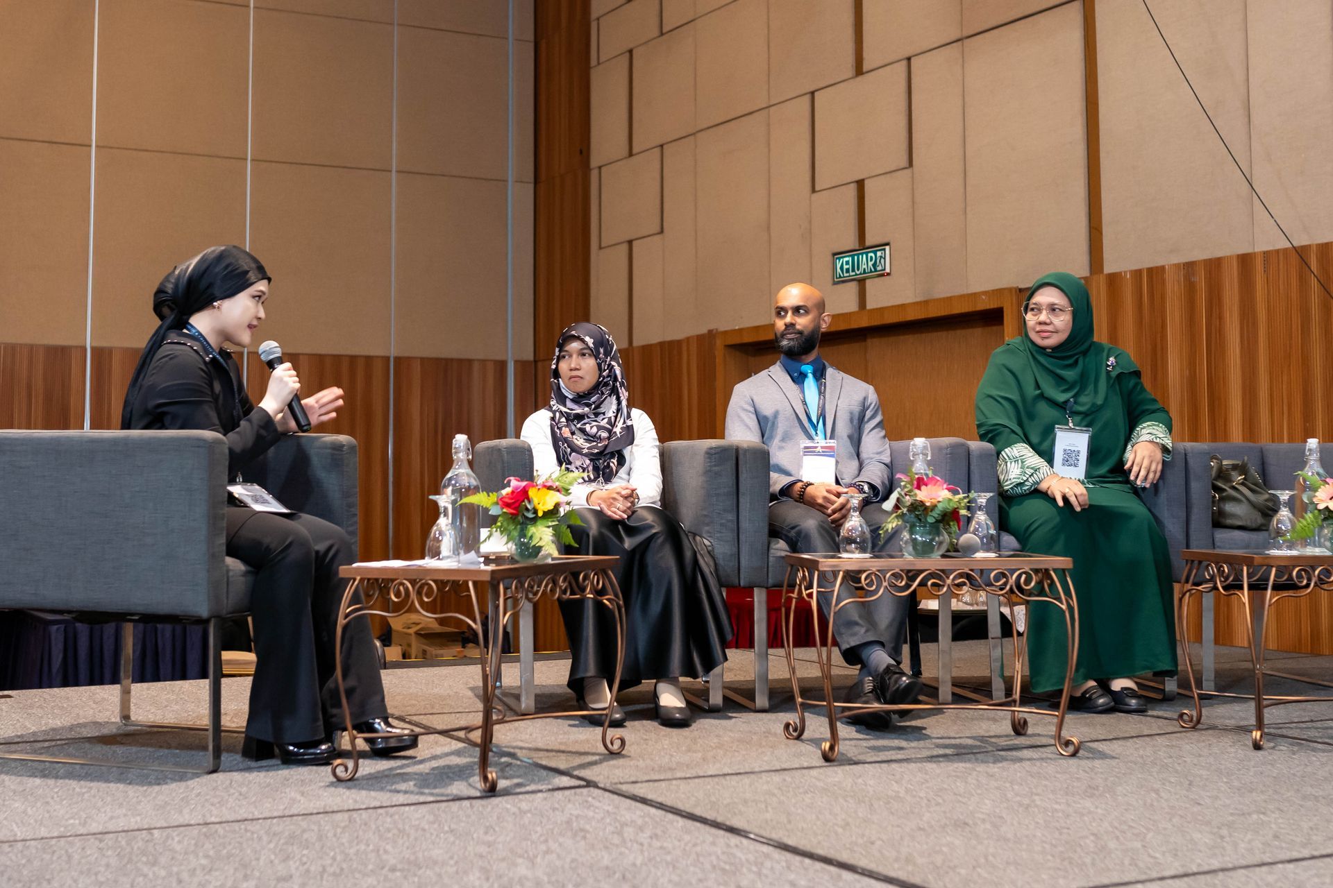 Panel discussion: four people seated on stage, talking into a microphone, with tables and flowers.