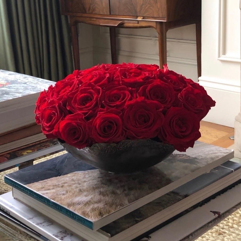 Preserved red roses in a metallic bowl on a stack of books,