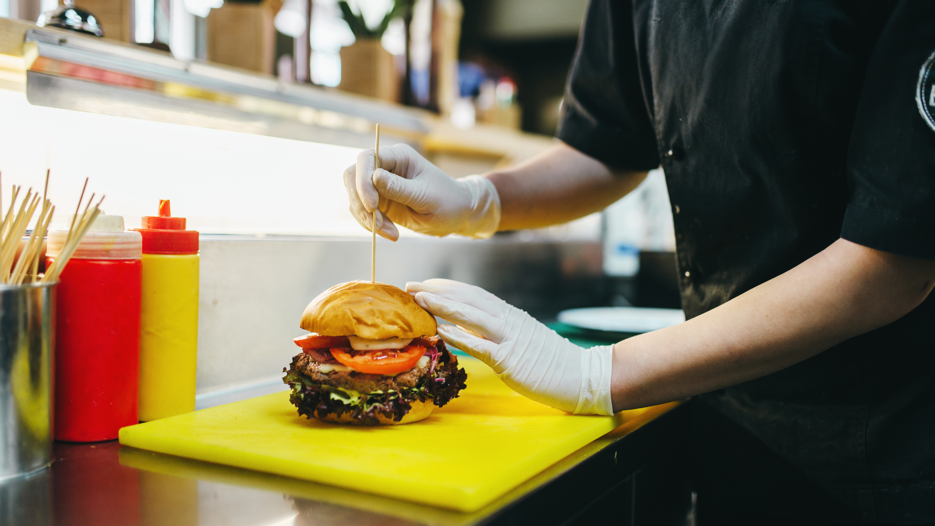 A person is making a hamburger on a cutting board in a kitchen.