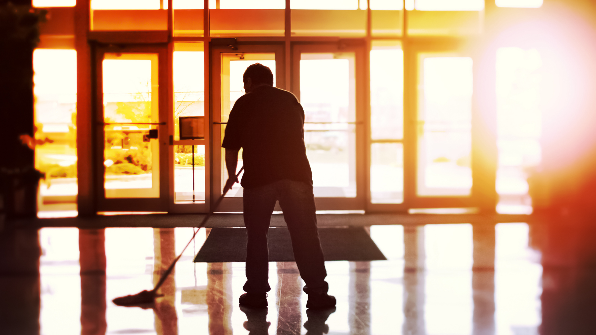 A man is cleaning the floor of a building with a mop.