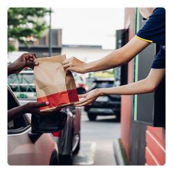 A person is handing a bag of food to another person from a fast food window. 
