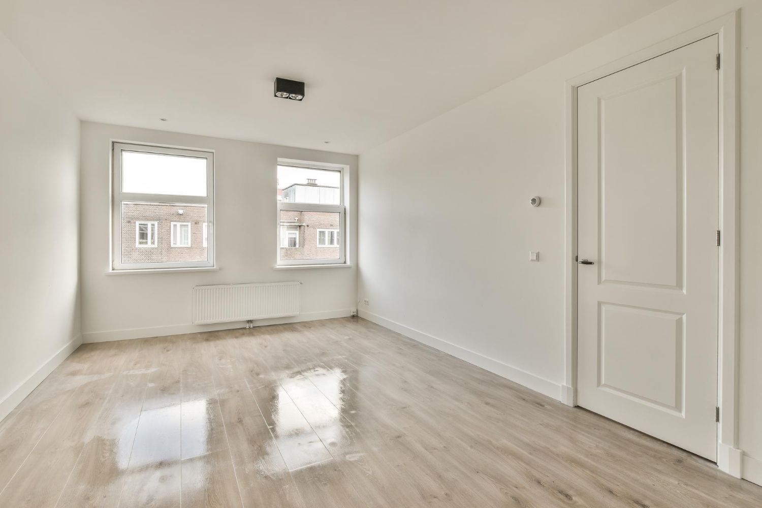 An empty living room with hardwood floors and white walls.