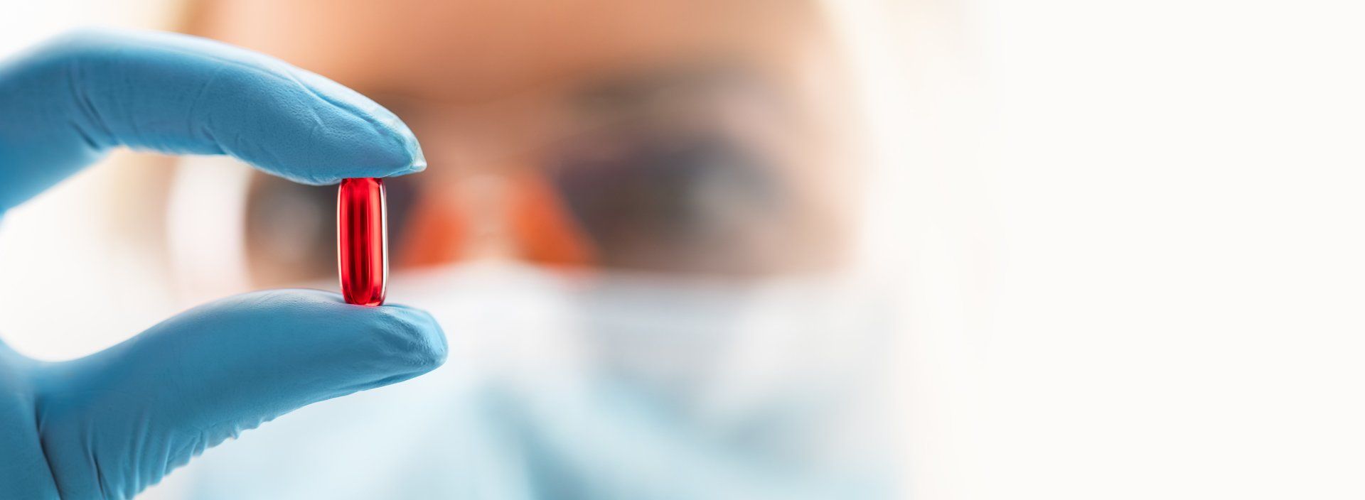A person wearing blue gloves is holding a red pill in their hand.