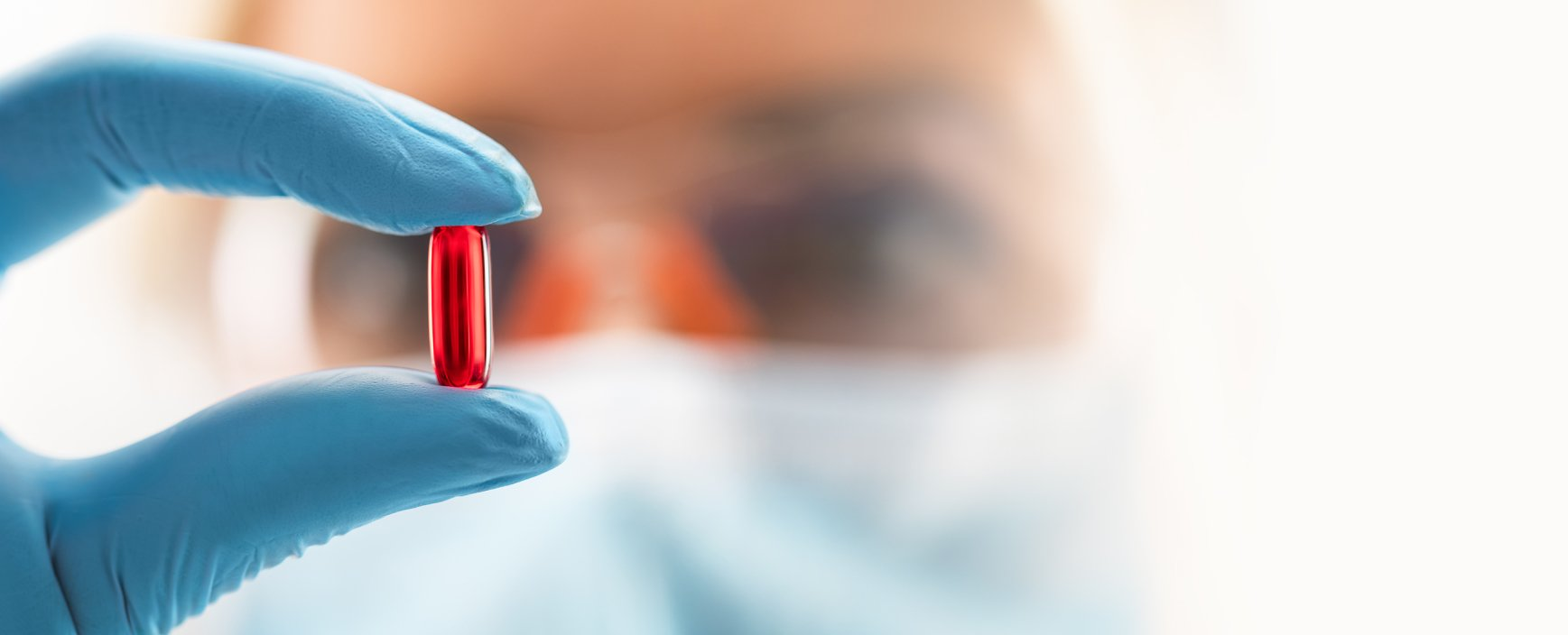 A person in a blue glove is holding a red pill in their hand.