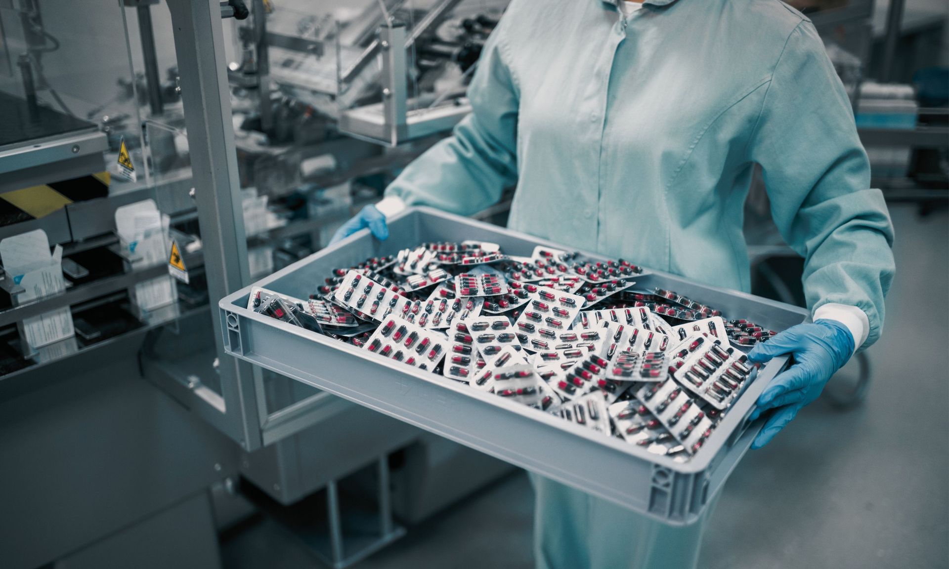 A woman in a clean room is holding a tray of pills.