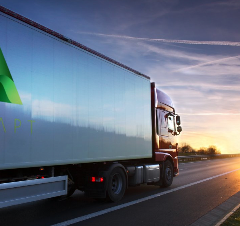 A semi truck is driving down a highway at sunset