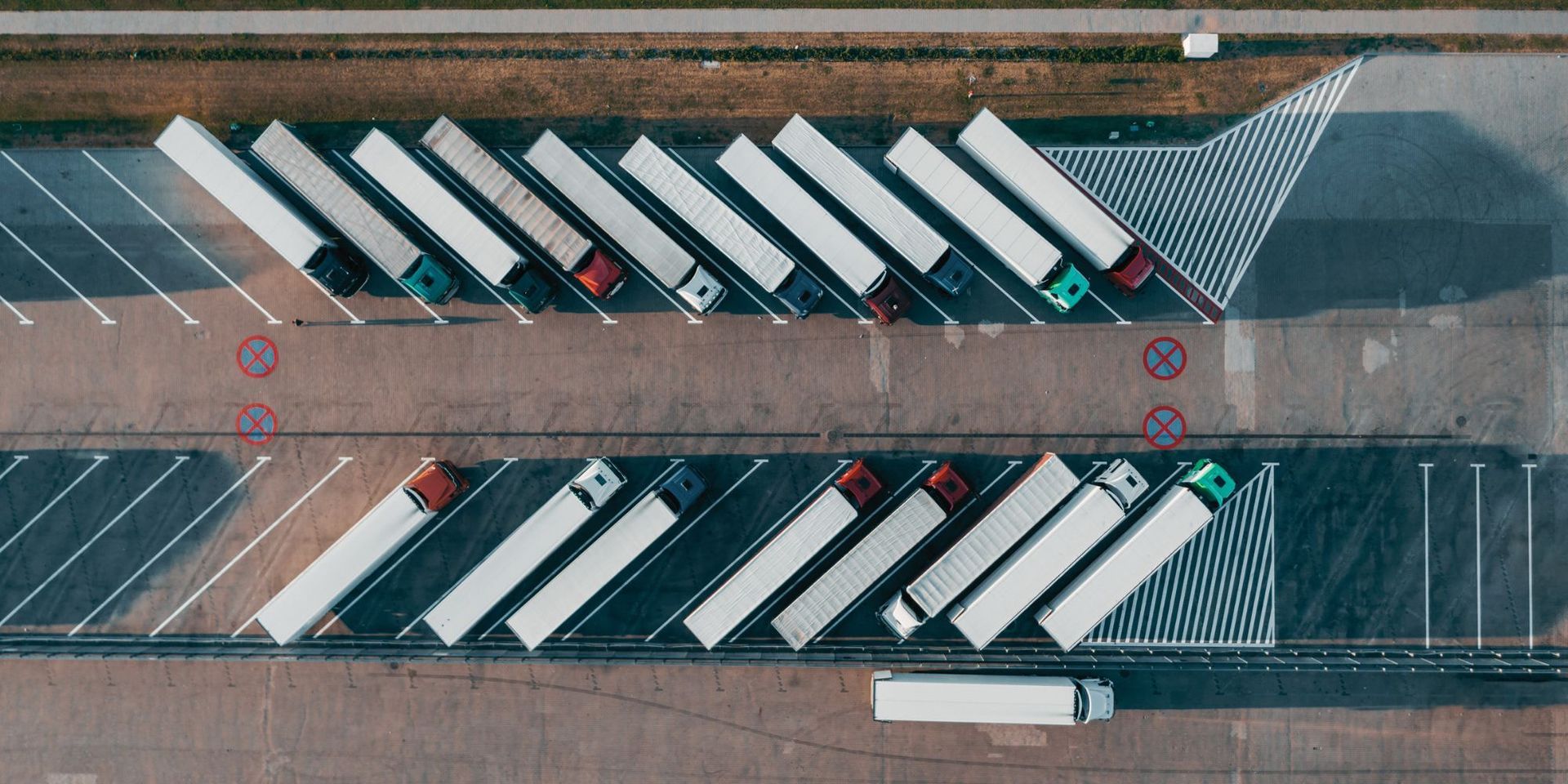Optimising transportation and logistics is crucial for achieving sustainability in the supply chain. An aerial view of a parking lot with trucks parked in a row.