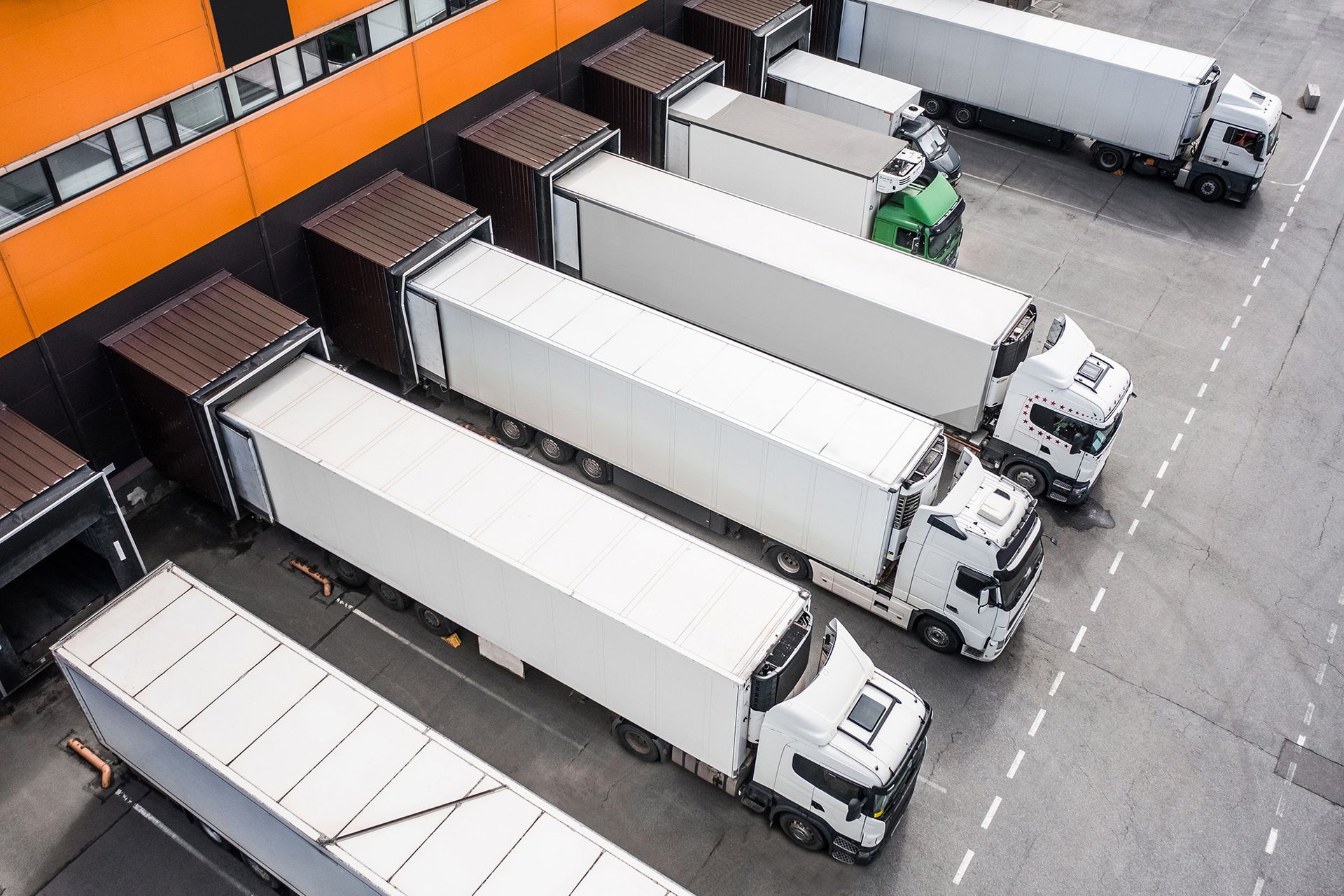 Loading Trucks Ariel View A row of white semi trucks are parked in front of a warehouse.