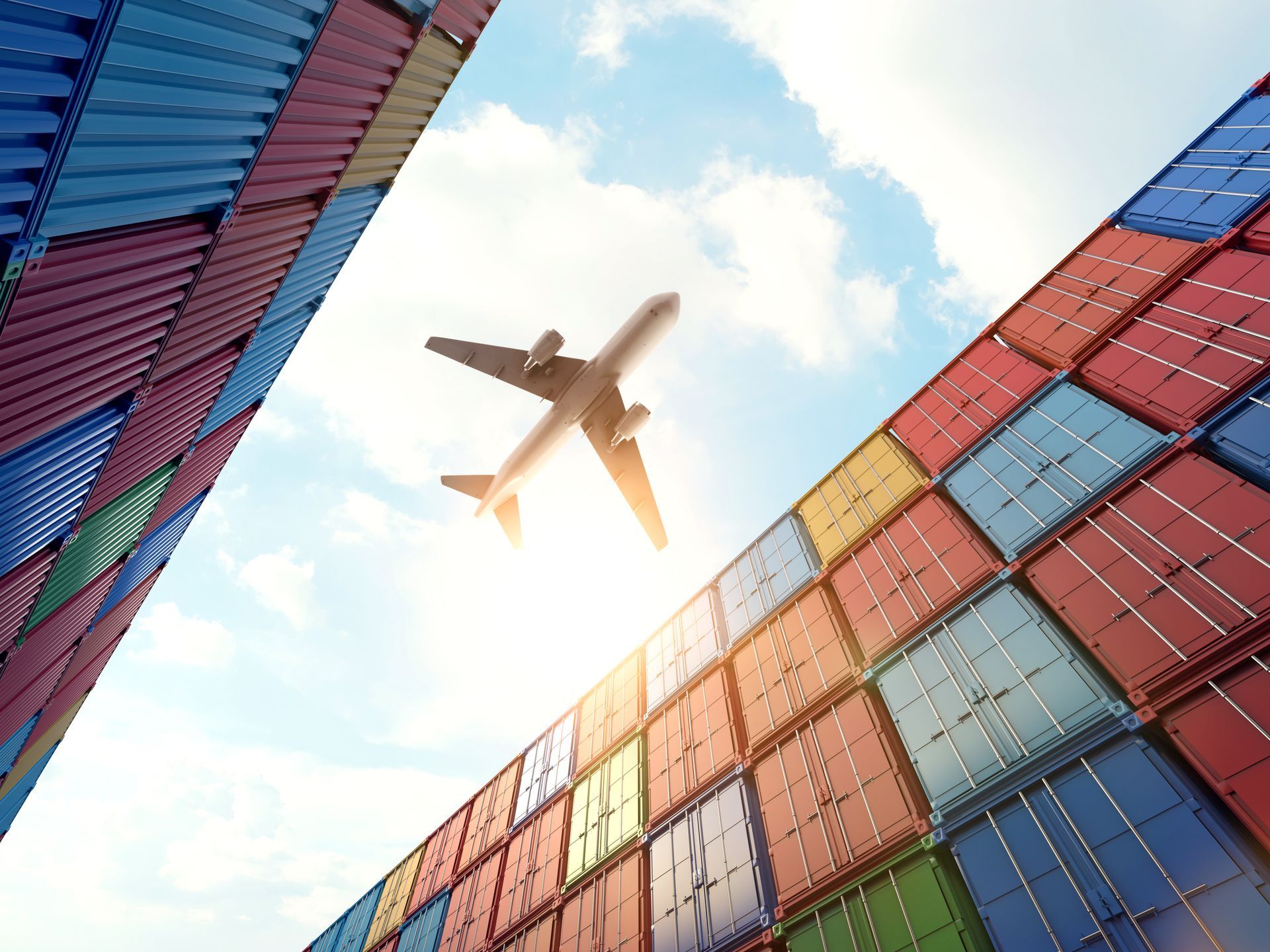 A plane is flying over a row of shipping containers.