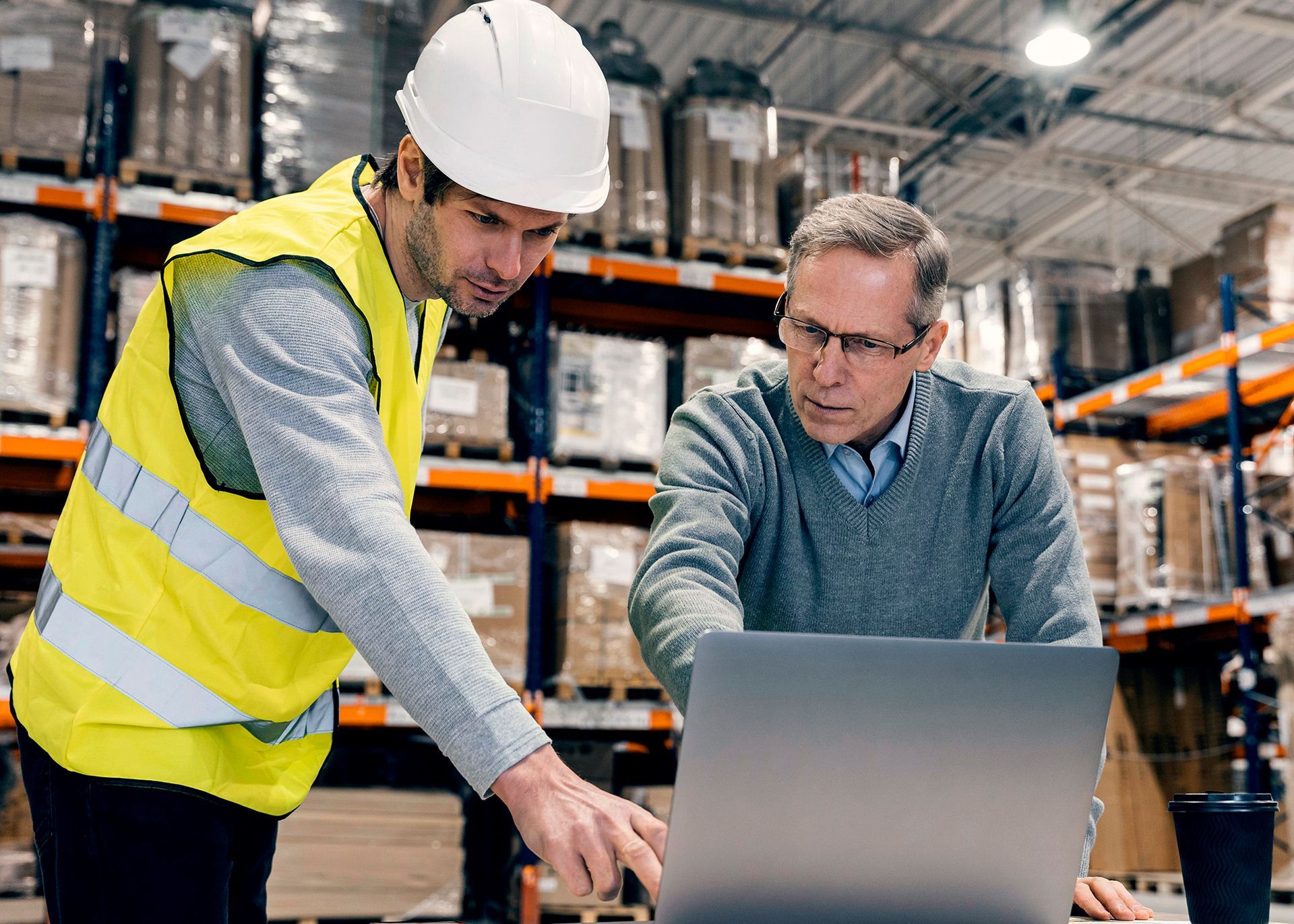 Two men are looking at a laptop computer in a warehouse.