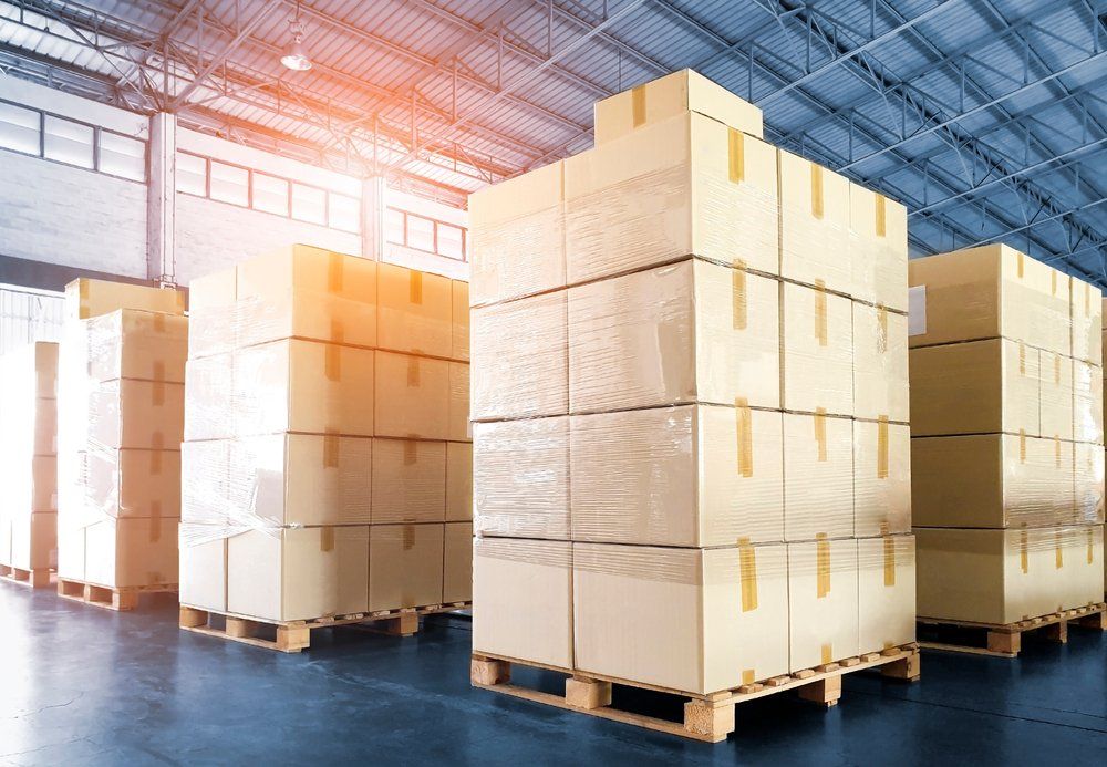 A warehouse filled with lots of cardboard boxes on wooden pallets.