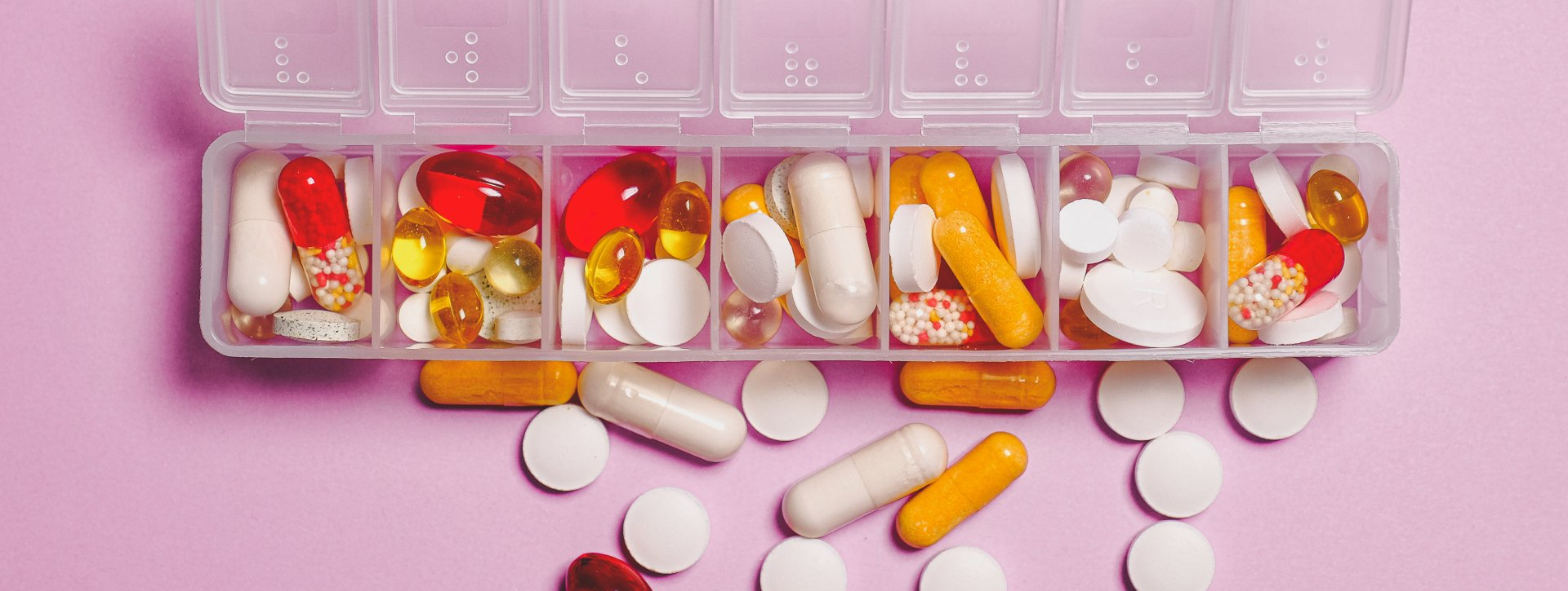 A box filled with pills and capsules on a pink background.
