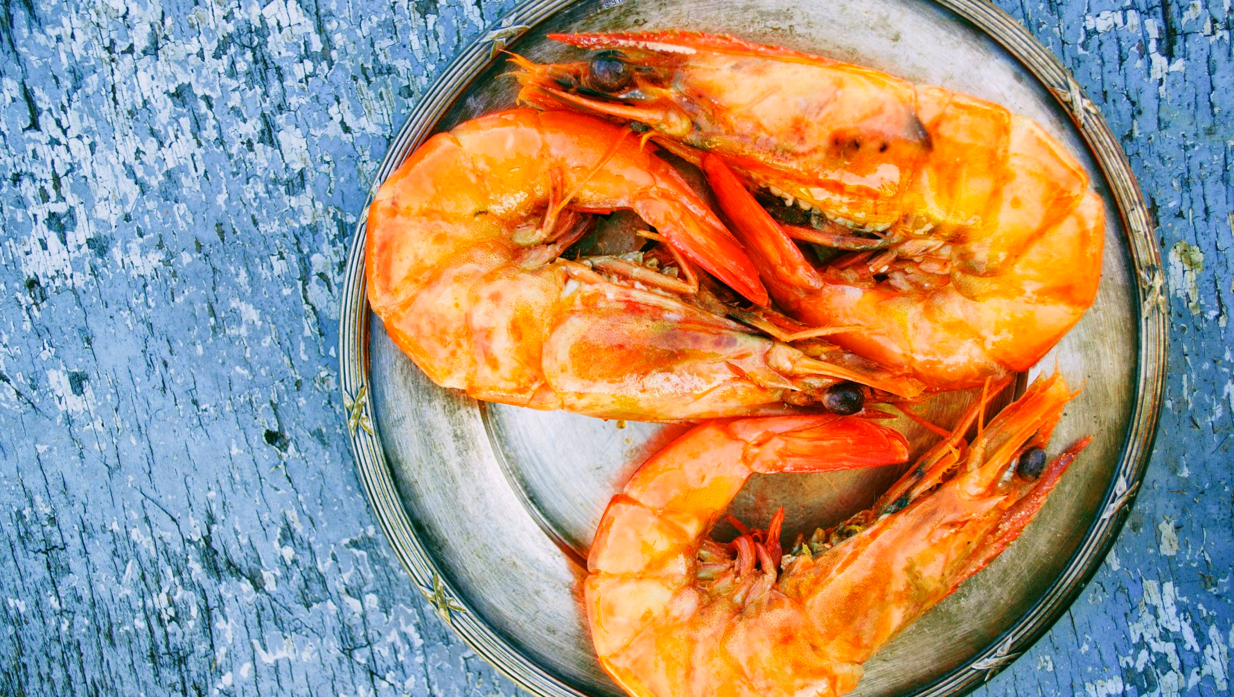 A plate of cooked shrimp on a blue table.