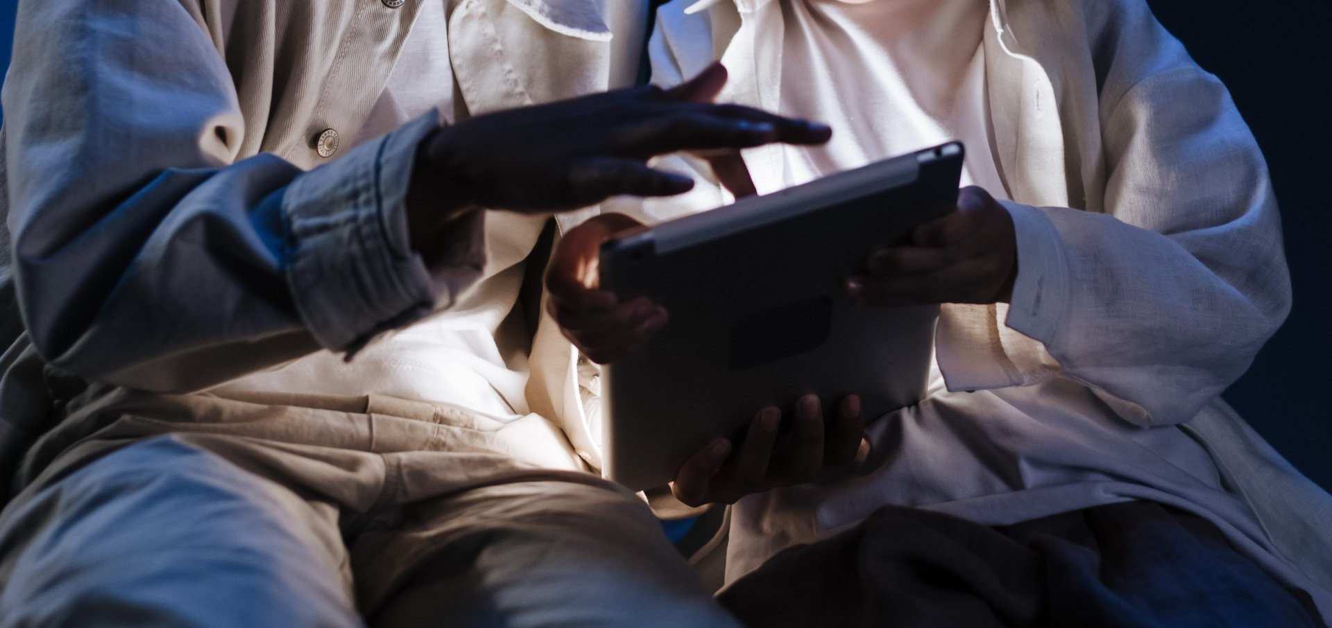 A man is sitting in a dark room using a tablet computer.