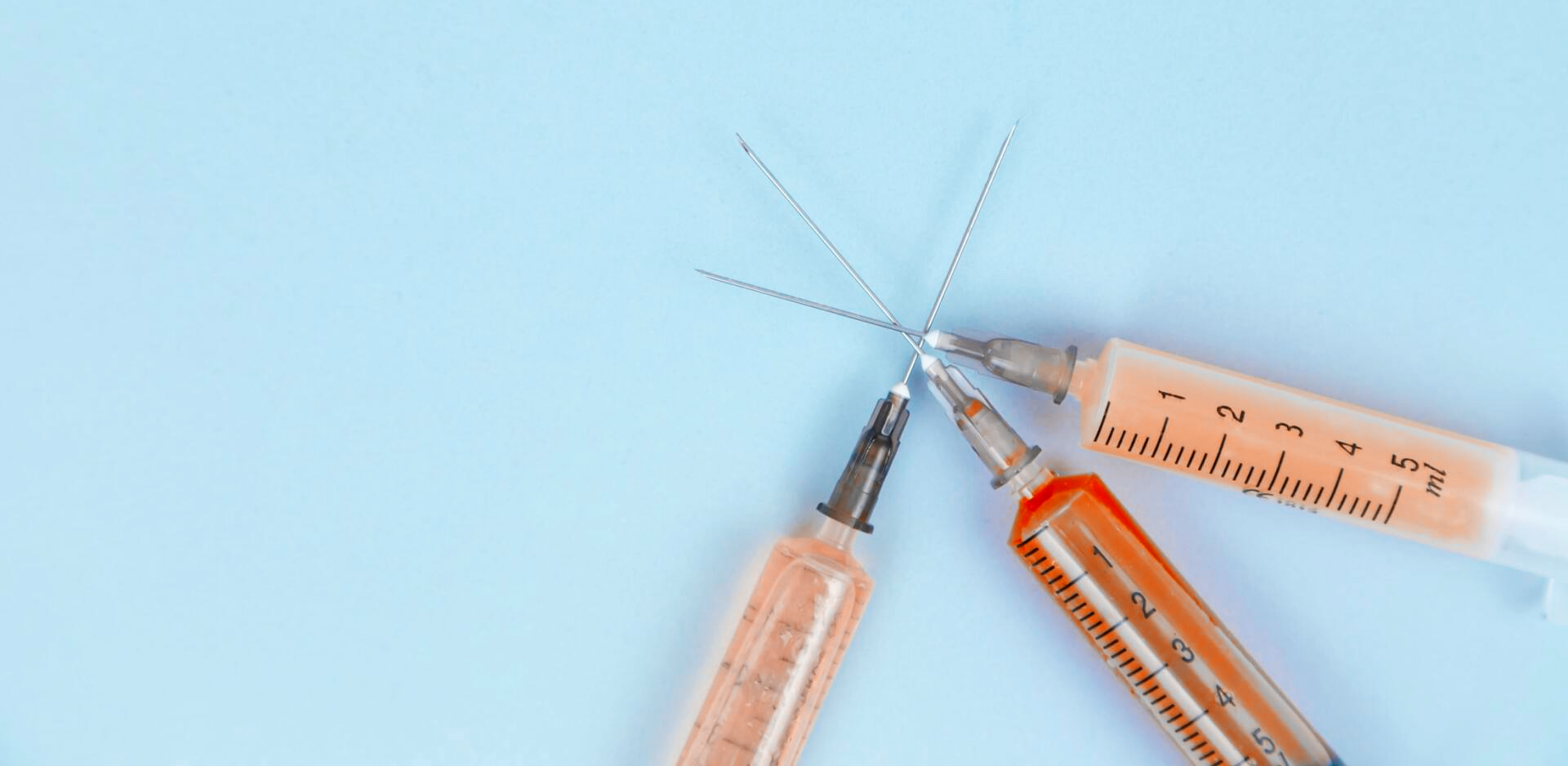 Three syringes are sitting on a blue surface.