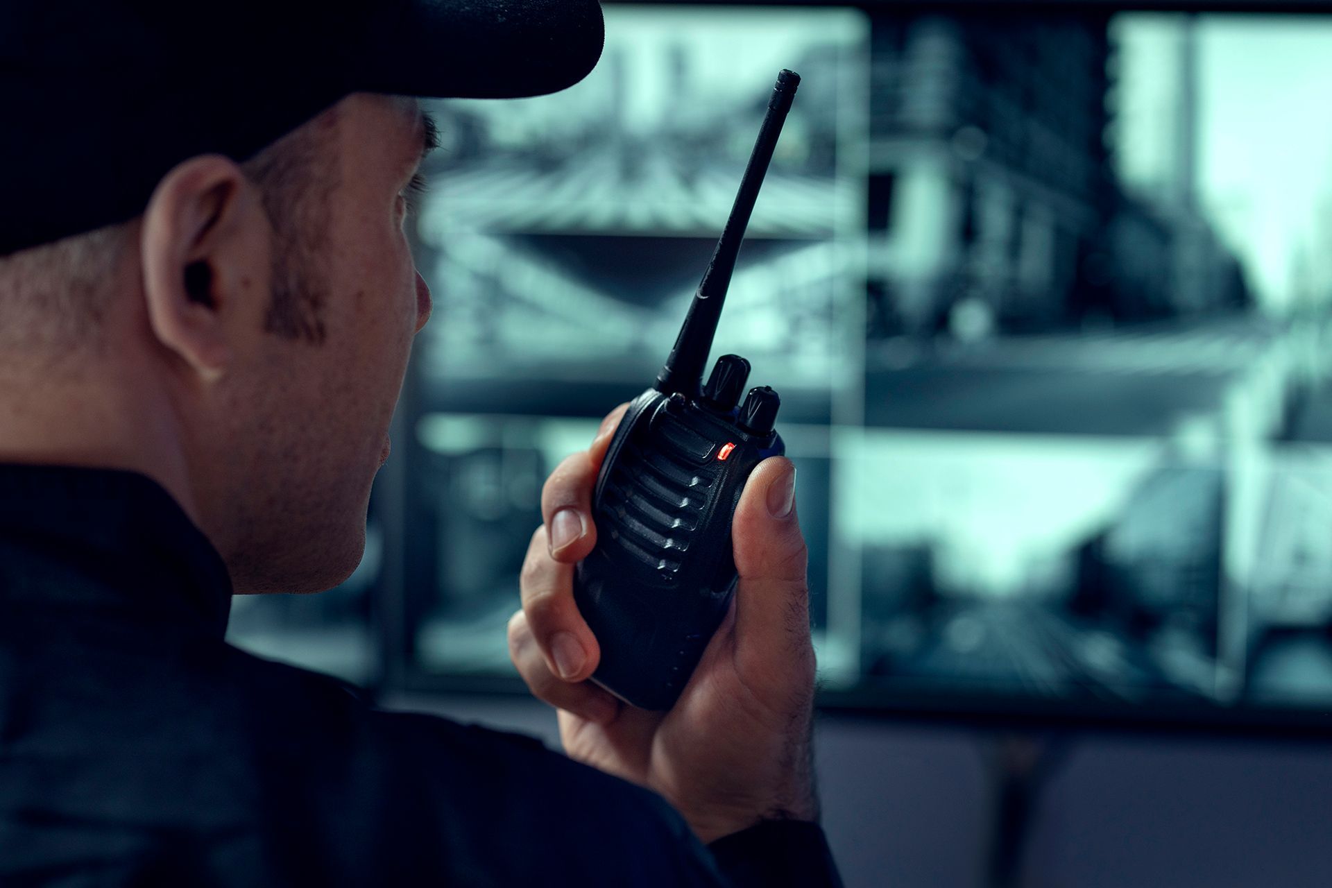 A security guard is holding a walkie talkie in front of a security camera.
