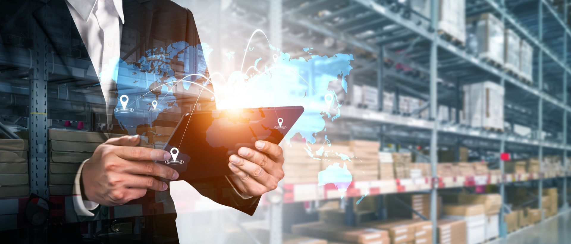A man in a suit is holding a tablet in front of a warehouse.
