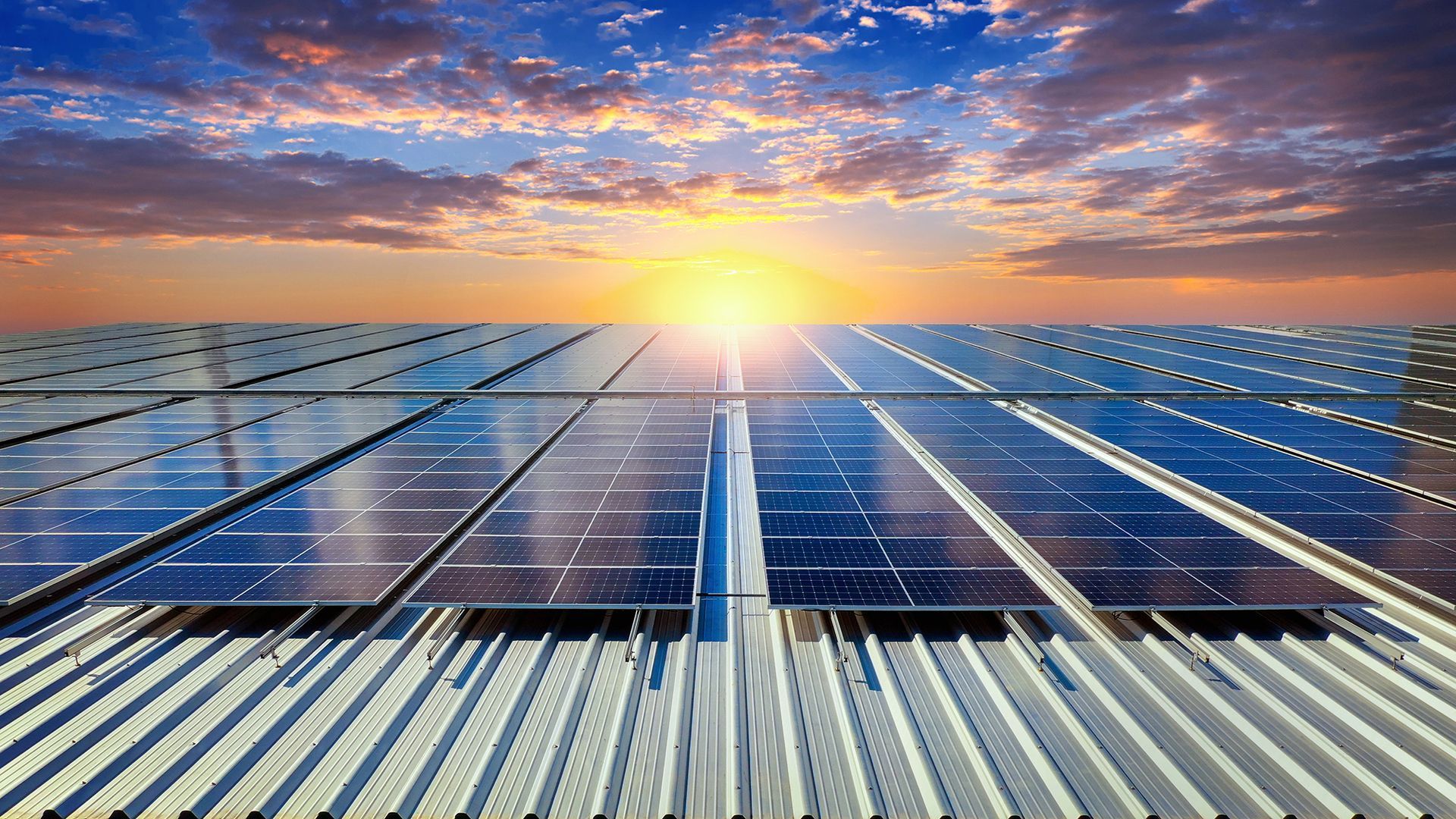 A row of solar panels on top of a metal roof at sunset.