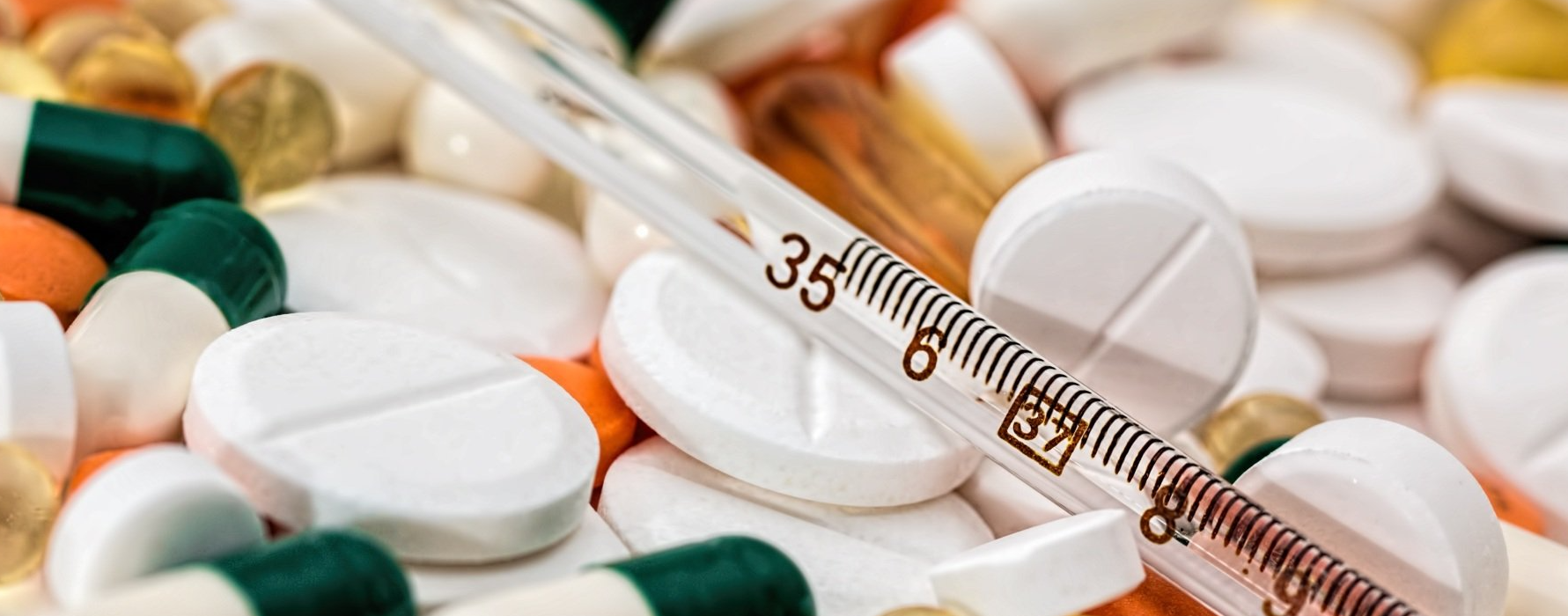 A thermometer is sitting on top of a pile of pills and capsules.