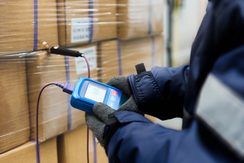 A man is using a thermometer to measure the temperature of a box in a warehouse.