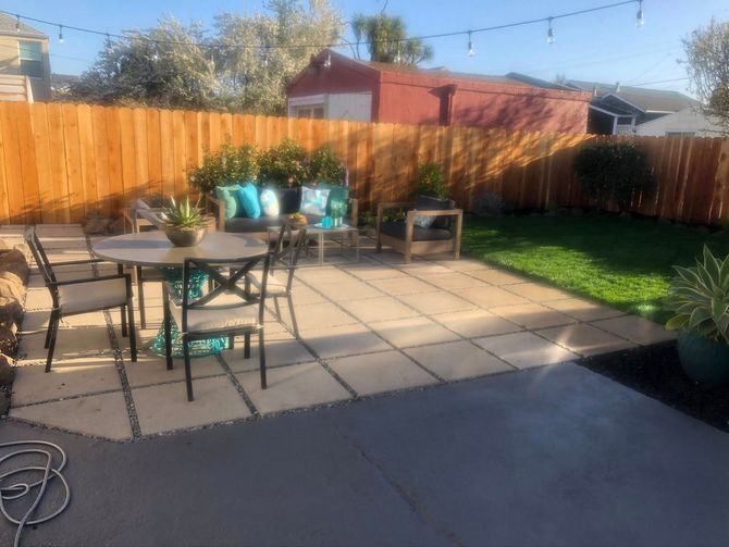 Backyard patio with table and chairs, potted plants, and a wooden fence in sunlight
