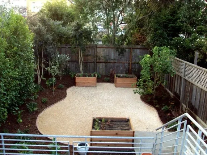 Backyard patio with gravel area, wooden benches, trees, and stairs leading down from a deck