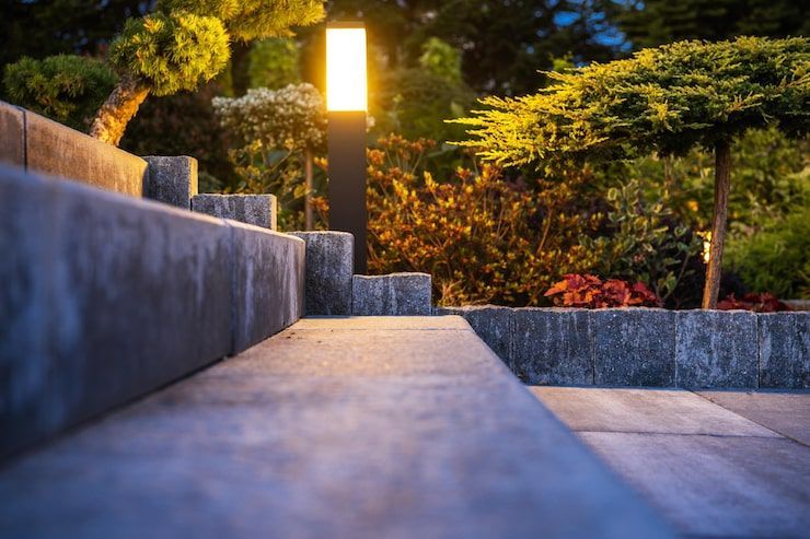 Lit stone walkway beside a glowing garden lamp and low wall at dusk