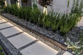 Modern garden bed with small shrubs beside stepping stones and gravel path