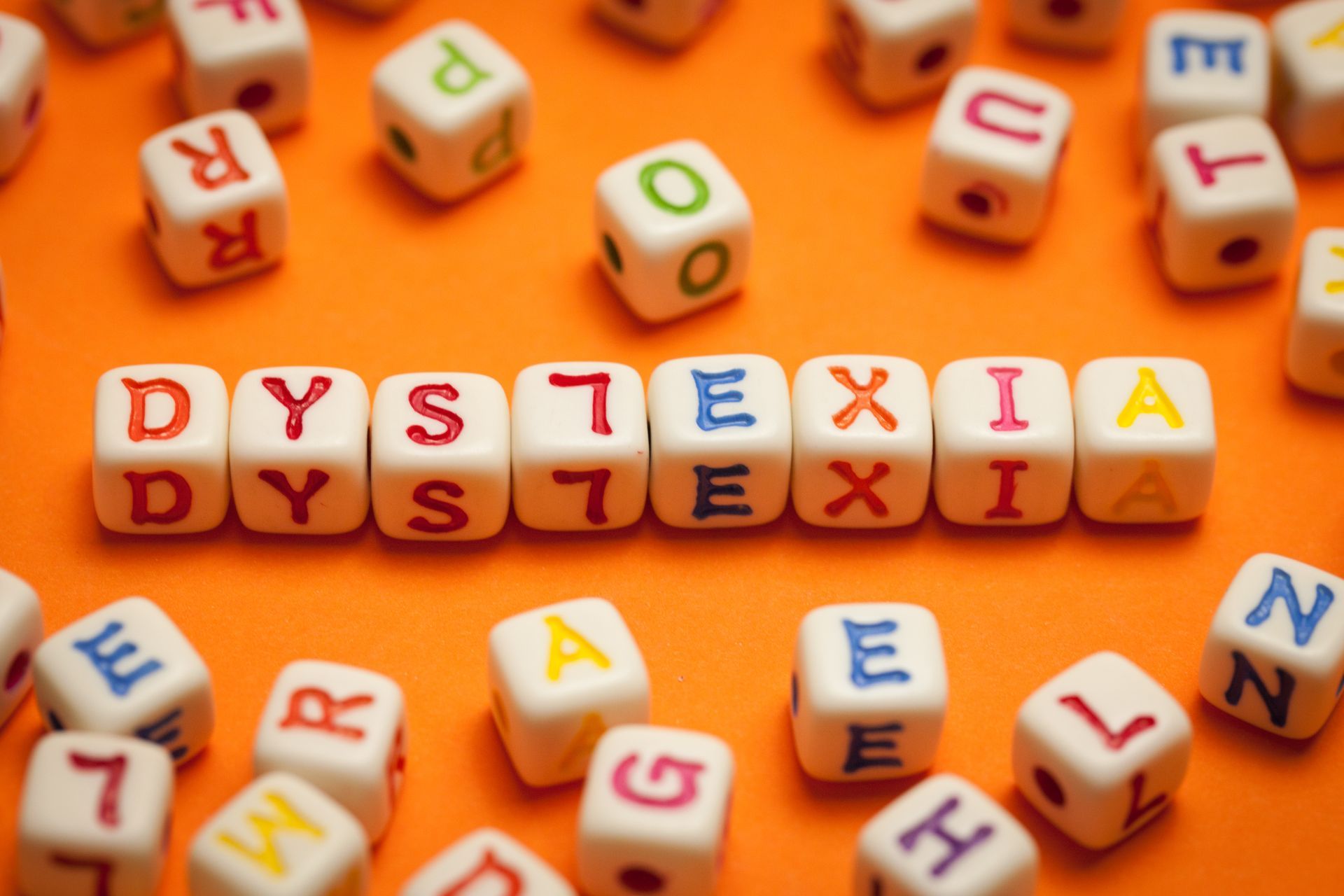 Colorful letter blocks spelling “DYSLEXIA” on an orange background