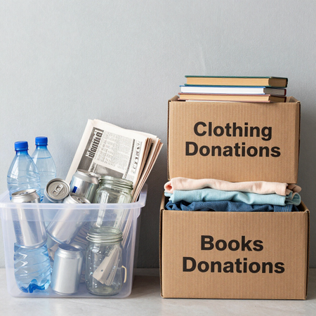 Clothing and books donation boxes beside a bin of water bottles and cans