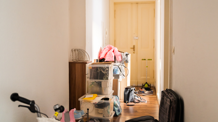 Cluttered hallway with boxes, a stroller, and coats leading to a closed wooden door