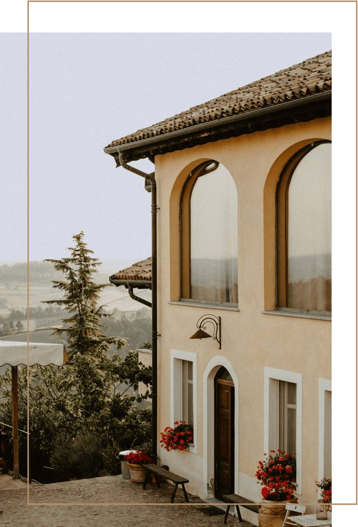 Beige building with arched windows, red flowers, and a scenic landscape view.