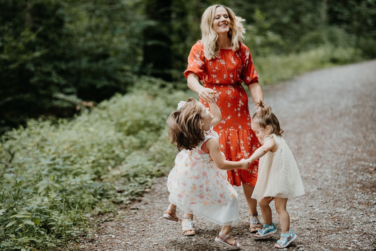 A woman in a red dress is walking down a dirt road with two little girls.
