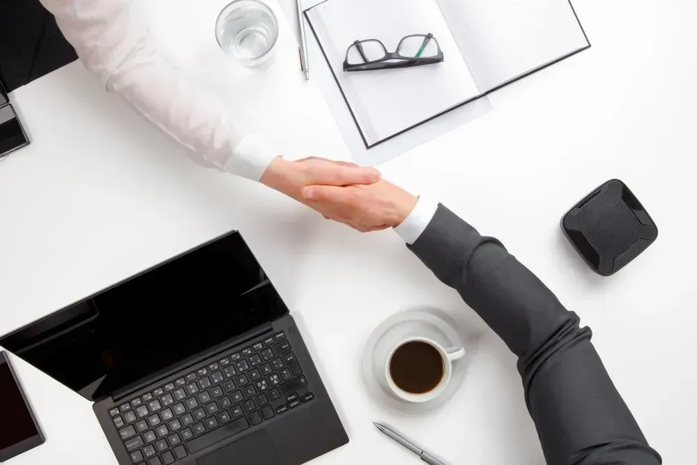 Two People in Business Suits Shaking Hands at A White Desk — Freedom Wealth Solutions in Mornington, VIC