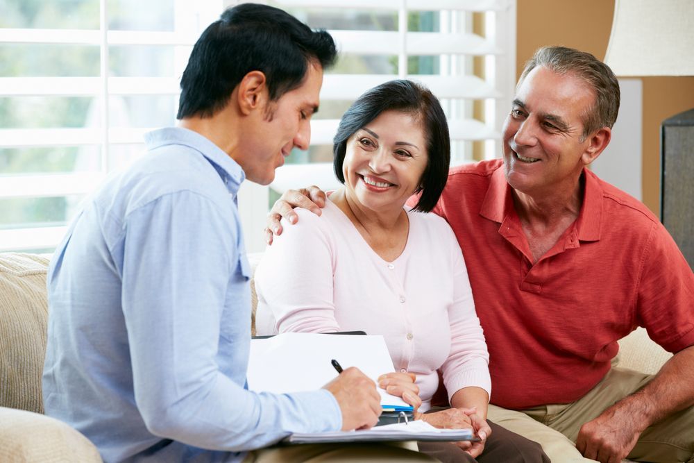 Man with Clipboard Talking to Smiling Couple in Living Room — Freedom Wealth Solutions in Mornington, VIC