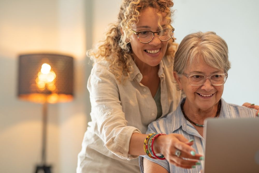 Woman with Curly Hair Points to Laptop Screen for Smiling Older Woman — Freedom Wealth Solutions in Mornington, VIC