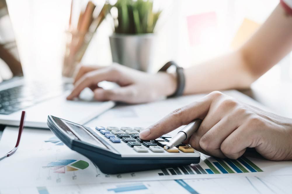Person Using a Calculator on A Desk with Papers, Charts, and A Laptop — Freedom Wealth Solutions in Mornington, VIC