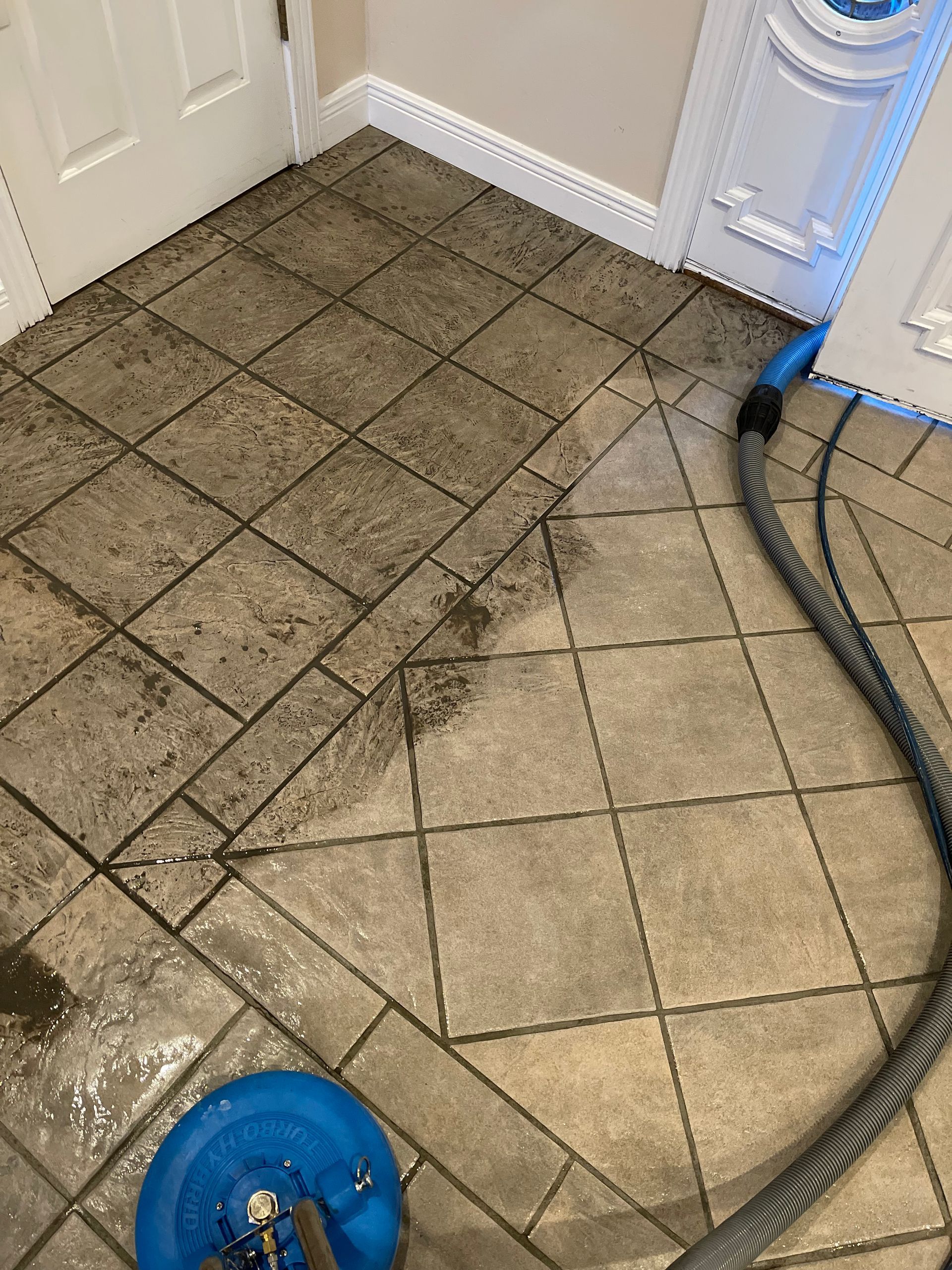 A tile floor being deep cleaned, showing a stark contrast between a dirty, dark section and a clean, light-colored area.