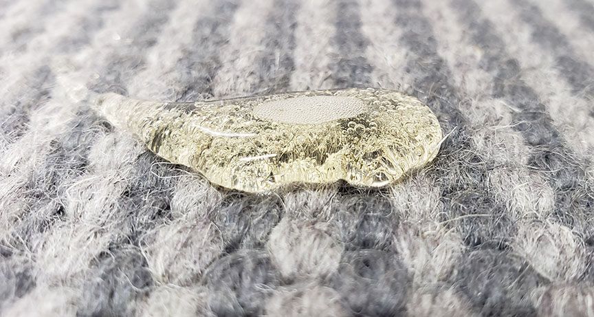 A small pale leaf resting on a gray patterned fabric surface.