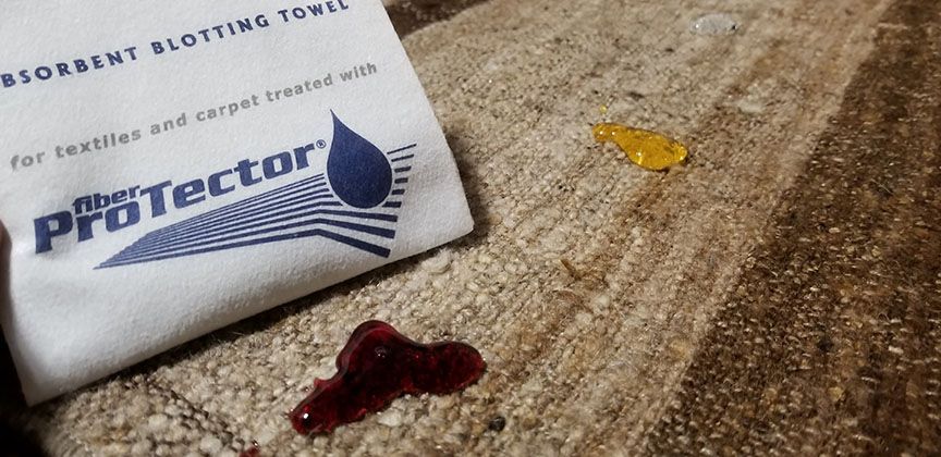 Paper towel blotting a small red spill on carpet next to a Pack of Protector pads
